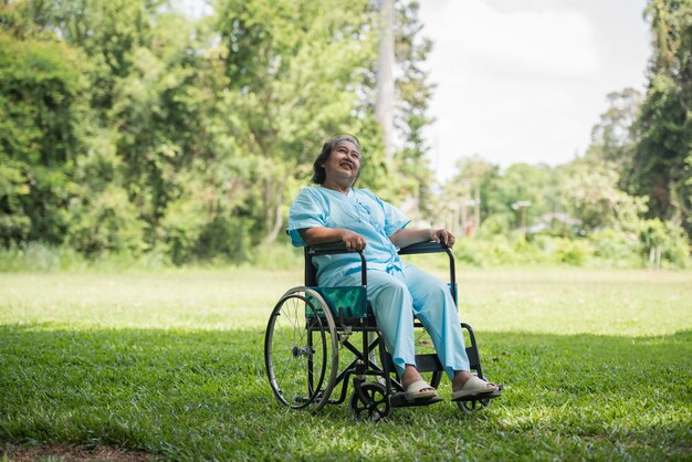 Mujer mayor sola que se sienta en la silla de ruedas en el jardín en hospital