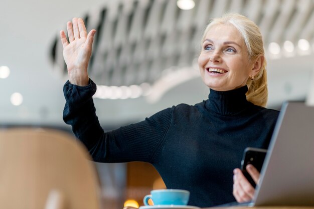 Mujer mayor sonriente pidiendo la factura mientras trabaja y toma un café