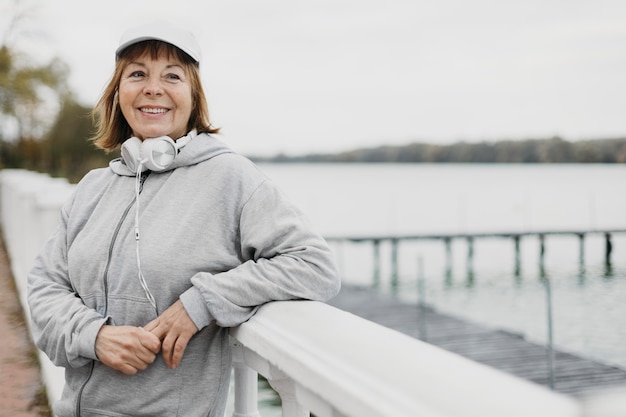 Mujer mayor sonriente posando al aire libre con auriculares mientras hace ejercicio