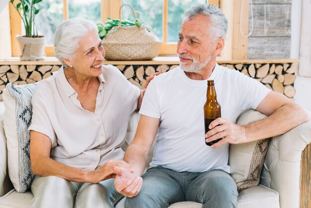 Mujer mayor sonriente que mira a su marido que sostiene la botella de cerveza