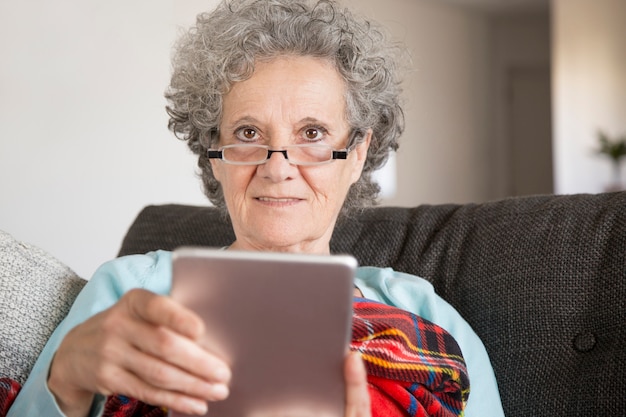 Mujer mayor sonriente en vidrios que lee noticias de Internet