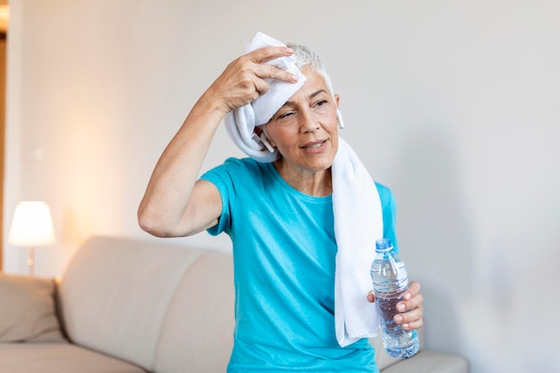 Mujer mayor sosteniendo una botella de plástico de agua limpiando el sudor con una toalla agotada después del entrenamiento diario