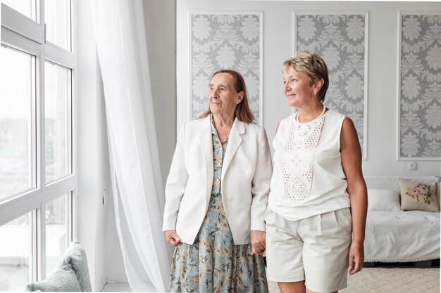 Mujer mayor y su hija madura mirando a la ventana