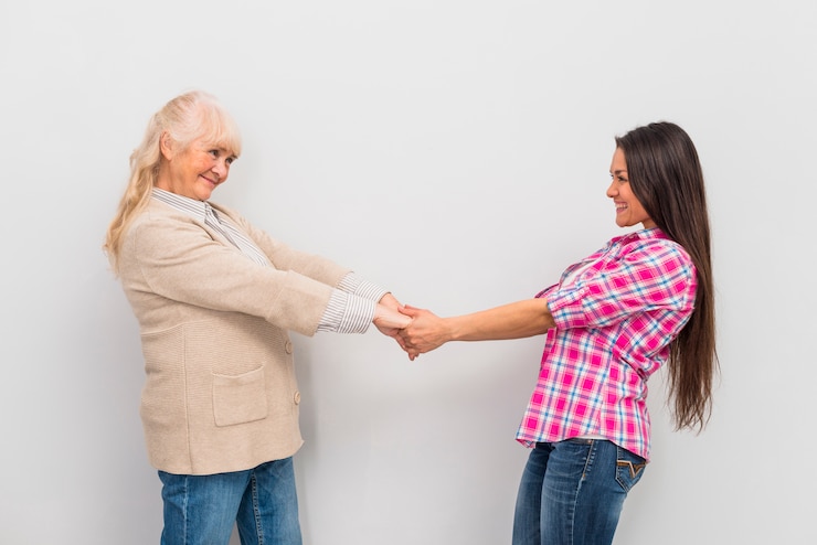 Foto gratuito mujer mayor y su hija de pie delante de la pared sosteniendo la mano del otro