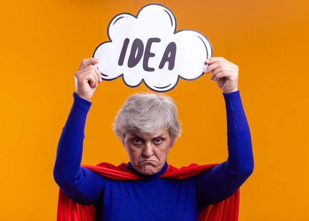 Mujer mayor superhéroe con capa roja sosteniendo el cartel de la burbuja del discurso con la idea de la palabra sobre su cabeza