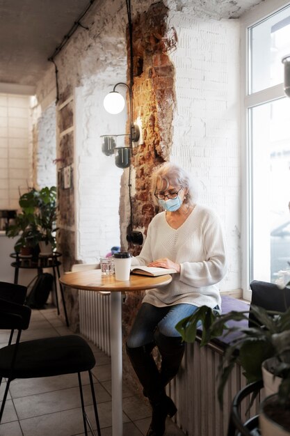 Mujer mayor de tiro completo leyendo en la cafetería