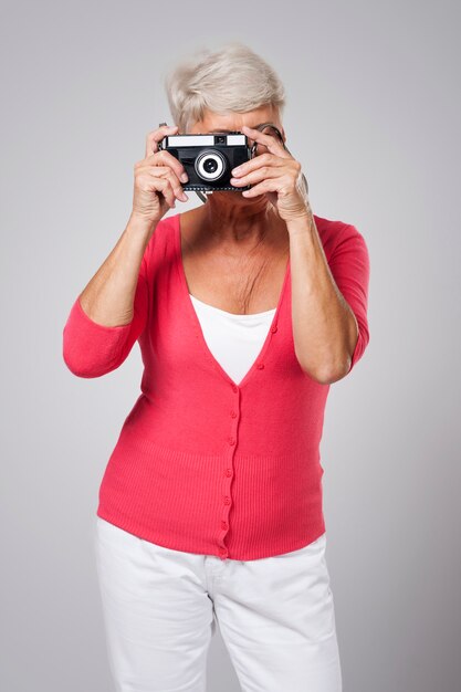 Mujer mayor tomando fotos por cámara retro