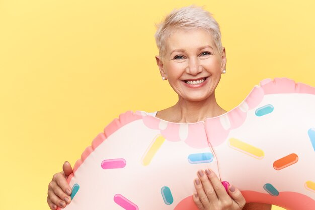 Mujer de mediana edad alegre enérgica posando aislada con círculo de natación inflable, yendo a relajarse en la piscina, sonriendo felizmente a la cámara, relajándose en el resort en horario de verano.