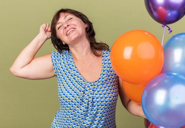 Mujer de mediana edad complacida con un montón de globos de colores levantando el puño feliz y emocionado