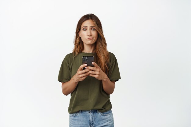 Mujer de mediana edad decepcionada y molesta con teléfono inteligente, cejas fruncidas y sonrisa con cara triste