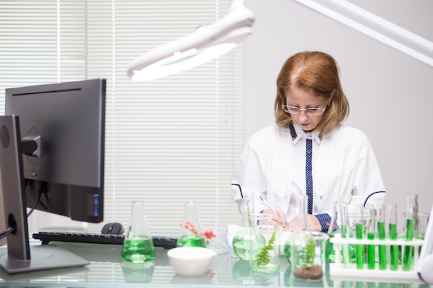 Mujer de mediana edad enfocada tomando notas después de la prueba científica en un laboratorio de producción. Biólogo trabajando.