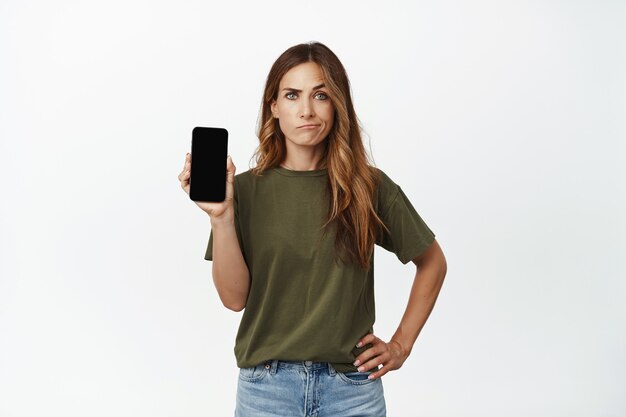 Mujer de mediana edad escéptica y molesta, madre mostrando la pantalla del teléfono móvil con cara de sonrisa insatisfecha