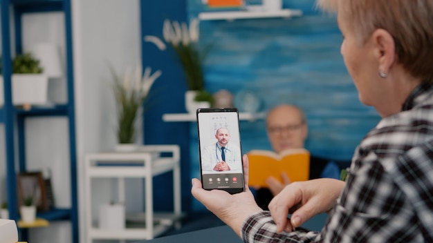 Foto gratuita mujer de mediana edad hablando en videoconferencia con el médico a distancia mediante un teléfono inteligente