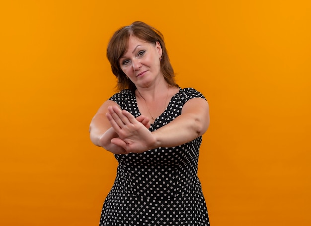 Mujer de mediana edad mirando seriamente haciendo gesto de parada en pared naranja aislada con espacio de copia