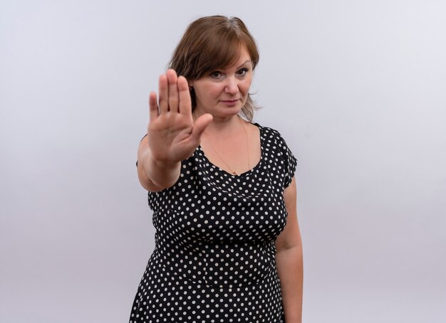 Mujer de mediana edad mirando seriamente que muestra la señal de pare con la mano en la pared blanca aislada