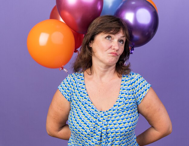 Mujer de mediana edad con montón de globos de colores mirando confundido