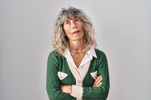 Mujer de mediana edad parada sobre fondo blanco con aspecto soñoliento y cansado, exhausta por fatiga y resaca, ojos perezosos por la mañana.