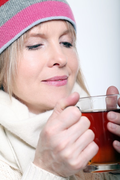 Mujer de mediana edad con té caliente vistiendo ropa de invierno sobre un fondo blanco.