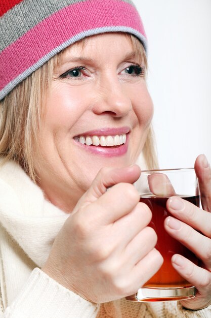 Mujer de mediana edad con té caliente vistiendo ropa de invierno sobre un fondo blanco.