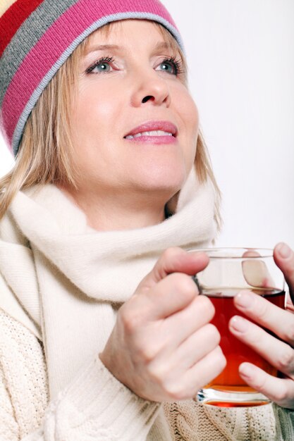 Mujer de mediana edad con té caliente vistiendo ropa de invierno sobre un fondo blanco.