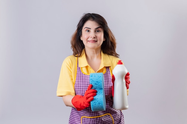 Foto gratuita mujer de mediana edad vistiendo delantal y guantes de goma con esponja y spray de limpieza