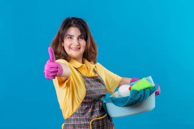 Mujer de mediana edad vistiendo delantal y guantes de goma sosteniendo el lavabo con herramientas de limpieza