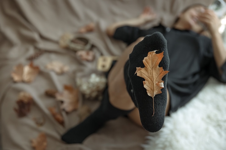 Foto gratuito una mujer con medias calientes sobre un fondo borroso y una hoja de otoño en foco.