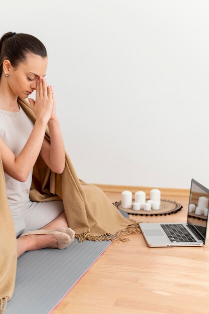 Mujer meditando en casa con un portátil al lado