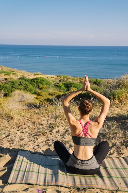 Mujer meditando en la playa vista trasera