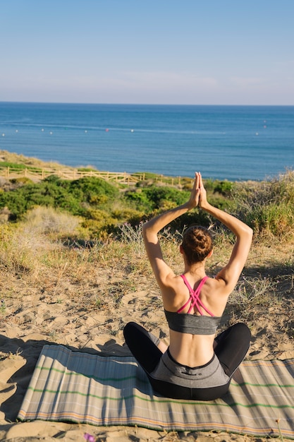 Mujer meditando en la playa vista trasera