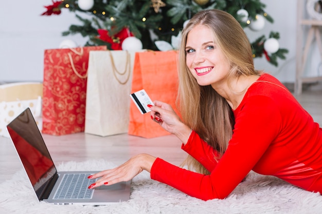 Mujer en la mentira roja en piso con la computadora portátil y la tarjeta