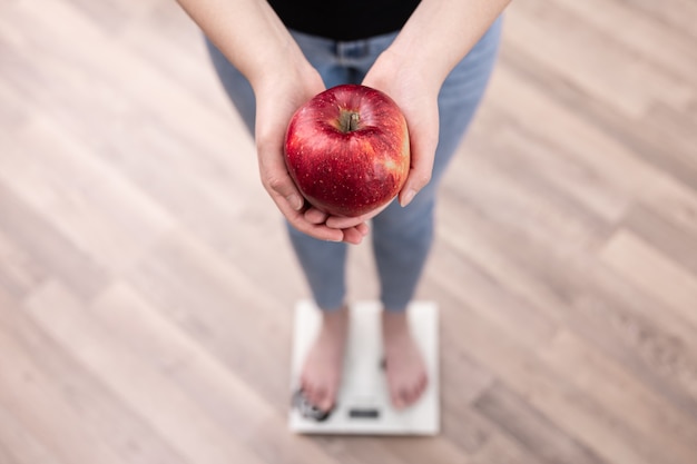 Foto gratuita una mujer mide el peso en una balanza, sostiene una manzana en sus manos.