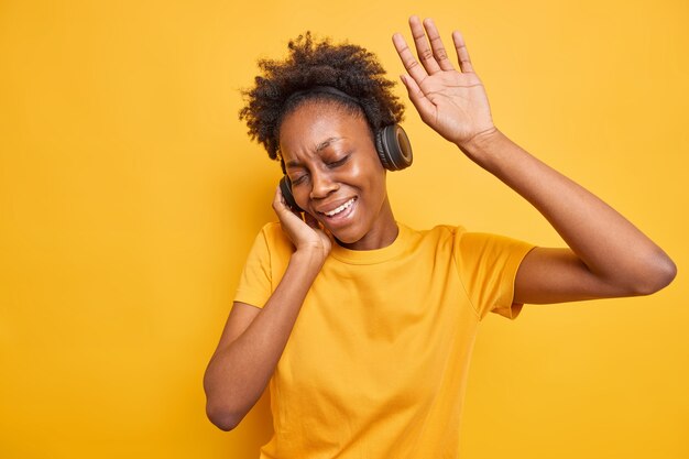 Mujer millennial de piel oscura despreocupada tiene movimientos divertidos con el ritmo de la música que mantiene el brazo levantado