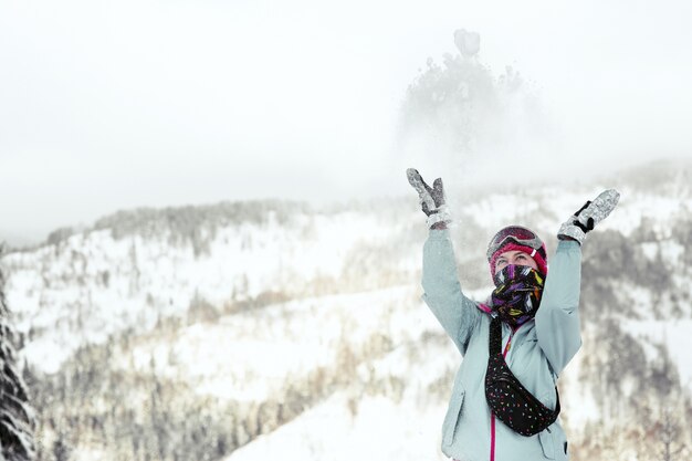 La mujer mira cómo cae la nieve en su cara mientras posa en la montaña de invierno