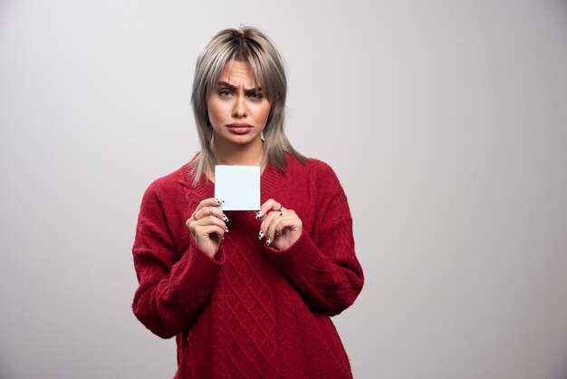 Mujer de mirada triste que sostiene el bloc de notas sobre fondo gris.