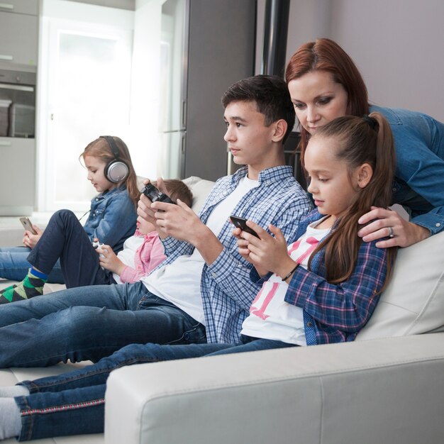 Mujer mirando adolescente y niña jugando videojuegos