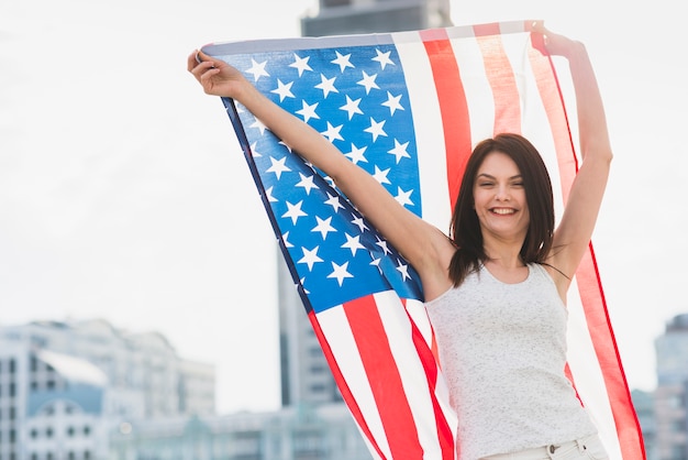 Mujer mirando a la cámara y riendo ondeando bandera americana ancha