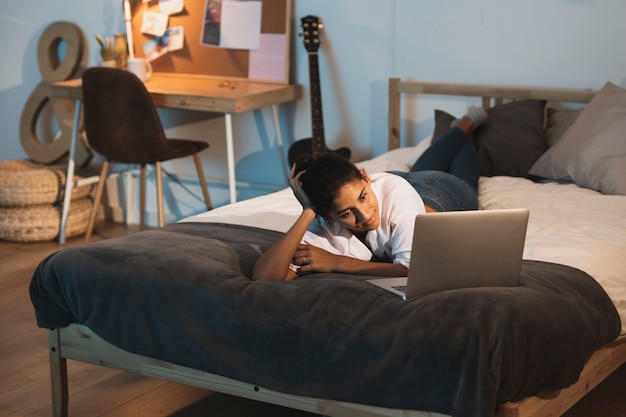 Foto gratuita mujer mirando en la computadora portátil y relajarse en la cama