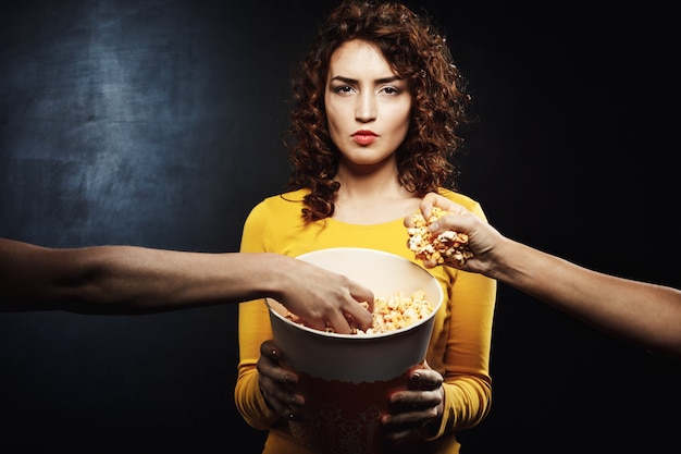 Mujer mirando directamente sosteniendo un cubo de palomitas de maíz mientras amigos agarran comida