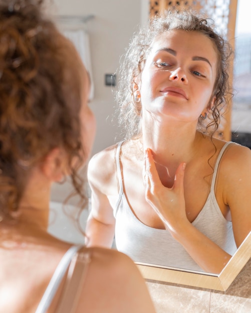 Mujer mirando en el espejo y aplicar crema en el cuello