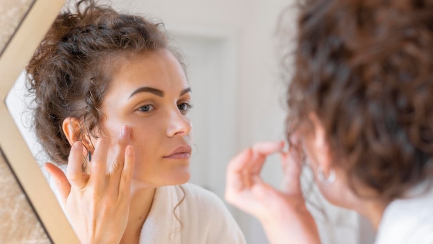 Mujer mirando en el espejo y haciendo rutina de belleza facial