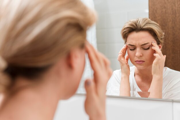 Mujer mirando en el espejo y teniendo dolor de cabeza