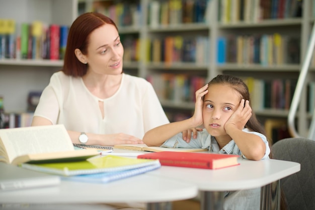 Foto gratuita mujer mirando inquisitivamente a una chica cansada estudiando en la mesa