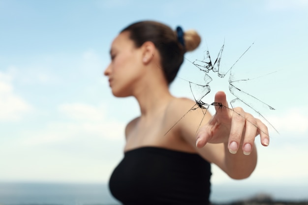 Mujer mirando a un lado mientras rompe un cristal con un dedo