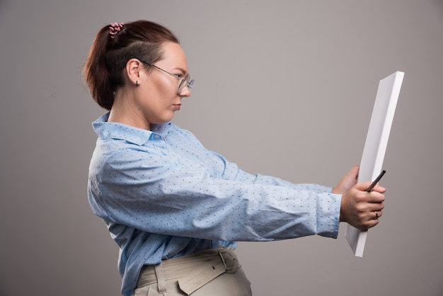 Mujer mirando lienzo vacío y pincel sobre fondo gris