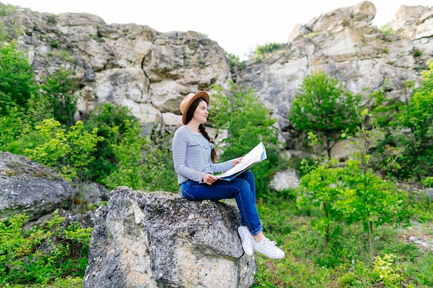 Mujer mirando a mapa sentada en una roca