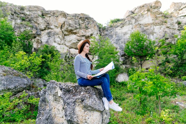 Mujer mirando a mapa sentada en una roca