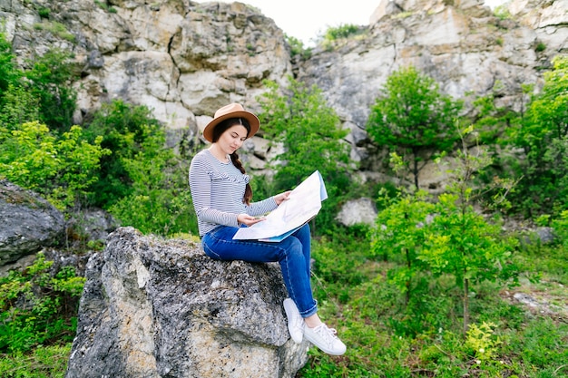 Mujer mirando a mapa sentada en una roca