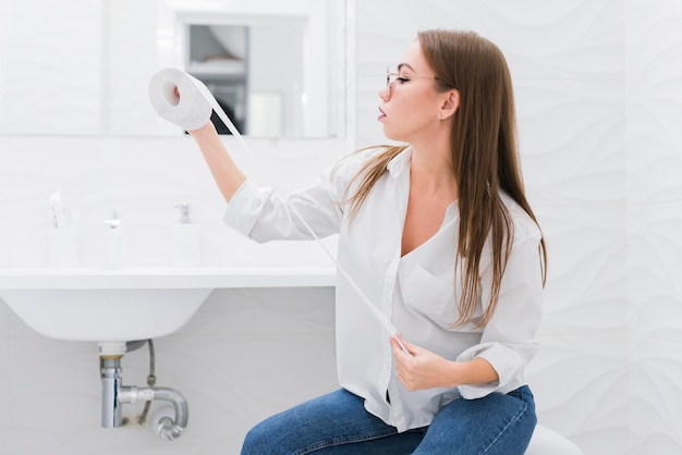 Mujer mirando un papel higiénico mientras está sentado en el inodoro