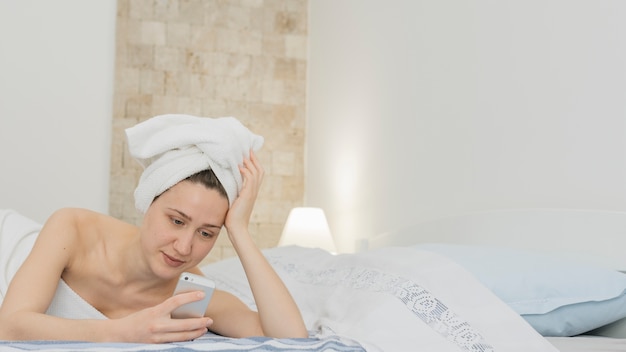 Mujer mirando a smartphone en la cama después de duchar